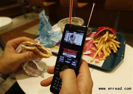 A man watches television through his mobile phone at a fast food restaurant in Tokyo July 10, 2009.